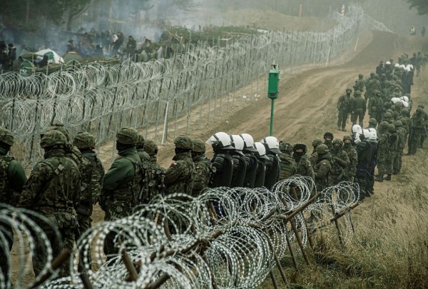 Polish soldiers and police watch migrants at the Poland/Belarus border near Kuznica, Poland, in this photograph released by the Territorial Defence Forces, November 12, 2021. Irek Dorozanski/DWOT/Handout via REUTERS  - pics/2021/11/58743_001_t.jpg